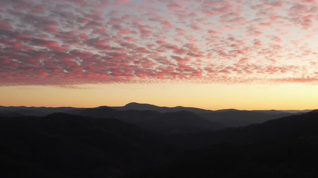 Stunning aerial view of pink altocumulus clouds at sunset over dark mountain ridges