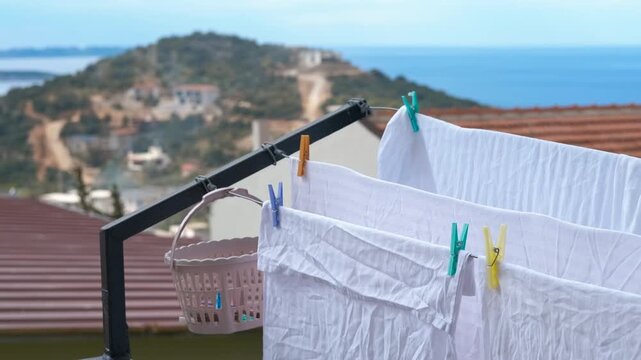 White laundry sheets hanging on clothesline drying in the sun. Freshly washed white sheets hanging on a clothesline, drying in the gentle breeze with a beautiful mediterranean village and sea view