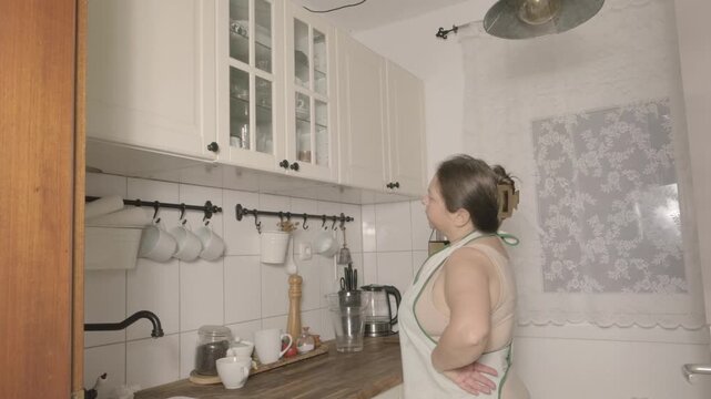 Woman in striped apron resting in kitchen after cleaning, tired but calm expression, domestic routine, housework, everyday life, concept rest, fatigue Break after housework, Everyday domestic routine