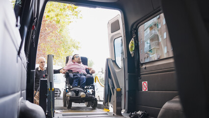 Man with disability entering a specialized van with assistance, utilizing a hydraulic lift for mobility and accessible transport © DMegias
