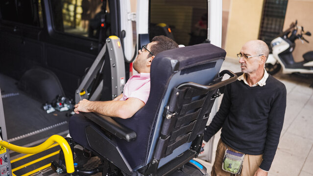 Man in wheelchair using a lift to enter an accessible van with assistance from a caregiver, promoting mobility and independence
