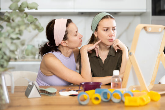 Adult and young women looking in mirror in kitchen at home..