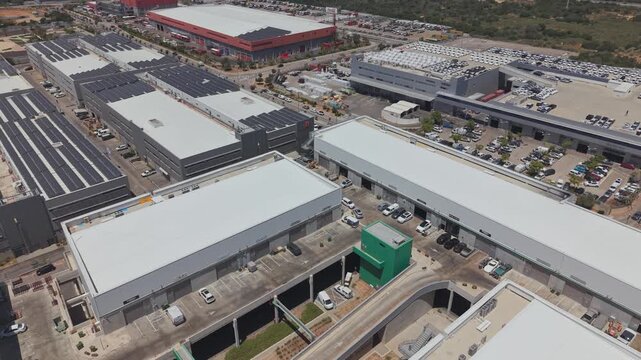 Aerial view of a large Israeli industrial park with warehouses, car dealership, solar panels and parking lots under clear blue sky
