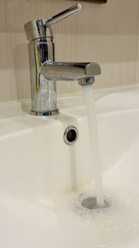 Dirty stainless faucet pouring water into unclean acrylic sink, visible mineral stains and soap scum around drain, slow steady