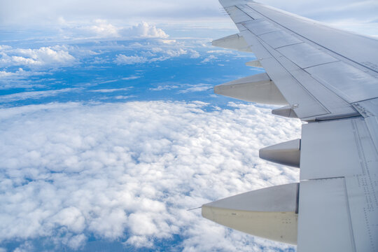 High altitude view of a white airplane wing over a dense layer of fluffy white clouds under clear blue sky during the day.