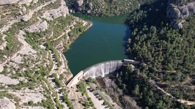 Backward reveal aerial shot of Margalef reservoir and dam on sunny winter day. Tarragona Province, Spain.