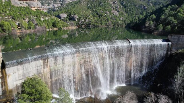 Forward reveal aerial shot of Margalef dam with water flowing through on sunny winter day. Tarragona Province, Spain.