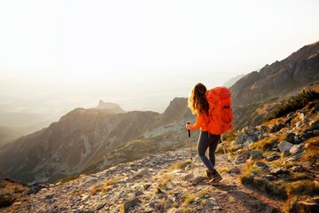 Obraz premium Orange backpack hiker walking on mountain trail background