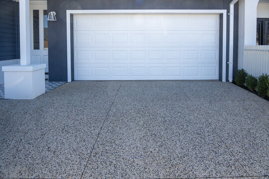 A modern white sectional garage door and exposed aggregate concrete driveway of a contemporary residential home in Australia. Curb appeal and premium suburban finishes