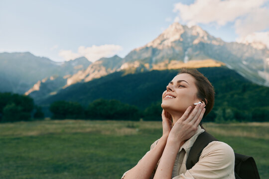 A young woman enjoys a peaceful moment outdoors with mountains in the background, eyes closed and hands gently touching her neck. Concept for lifestyle, relaxation, and nature.