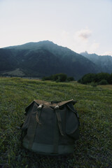 Obraz premium Rugged backpack resting in a grassy field with distant mountains, an outdoor lifestyle scene that conveys adventure, solitude, and simple travel gear in natural light