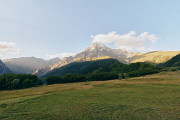 Fototapeta premium Tranquil meadow with rolling hills and distant mountains under a clear blue sky, a calm outdoor landscape ideal for nature lovers and travel storytelling and tranquil mood.