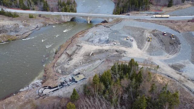 Drone aerial footage of the future Arthur-Bergeron bridge construction site as trucks cross the old bridge above the Mitis River near the St. Lawrence River in Quebec, Canada.