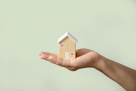 Hand holding wooden house model soft green background. Home ownership, property management, real estate insurance, homeless, foster home care