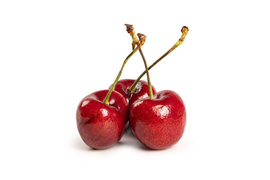 Three vibrant, glossy red cherries at the stem isolated on white background.