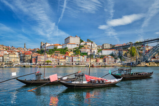 Porto rabelo boats moored on Douro River beside Ribeira, Portugal, with traditional wooden boats, wine barrels and Vila Nova de Gaia riverfront