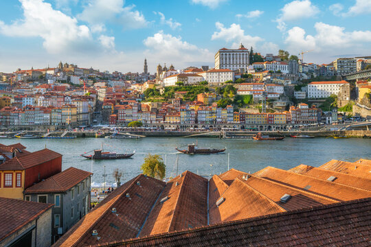 View of Porto Ribeira, Portugal, across Douro River over house rooftops, with tourist rabelo boats on the Douro River and red rooftops in the foreground