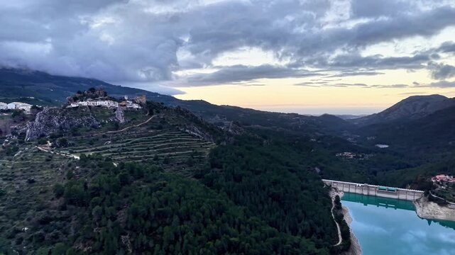 Sunset hilltop village overlooking turquoise reservoir, terraced slopes and vineyard patches cascade