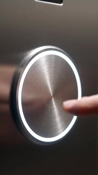 Close up of a finger pressing a lit circular button on a metallic surface representing technology and interaction with modern interfaces