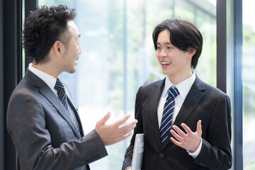 新緑のオフィスの窓際で会話する若手ビジネスマンと上司、取引先のコミュニケーション商談と成長の仕事イメージ © kapinon