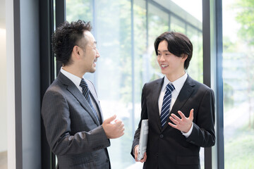 新緑のオフィスの窓際で会話する若手ビジネスマンと上司、取引先のコミュニケーション商談と成長の仕事イメージ © kapinon