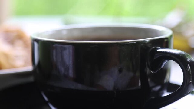 A cup of hot black coffee with a thin steam rising from it