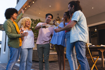 Diverse group raising glasses and pouring from champagne bottle on covered patio with string lights © wavebreak3