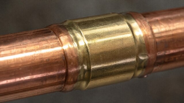 flippant. Close-up of a shiny brass joint connecting two copper pipes. safety posters, maintenance manuals, designed for industrial assembly lines and welding operations, used by engineers.