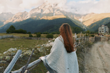 Obraz premium Outside scene with a woman seen from behind, wearing a cozy cardigan, gazing toward distant mountains, a relaxed lifestyle moment in natural light.