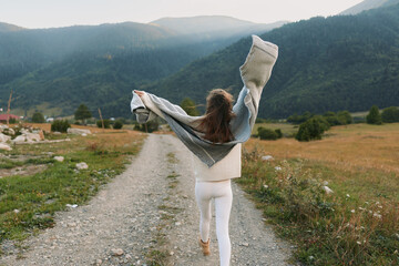 Obraz premium A woman on a rural path raises her arms in joy, embracing freedom and nature. Open landscape, open road, and fresh air capture a carefree lifestyle moment outdoors.