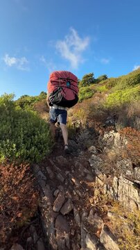 A Hiker Climbs a Rocky Trail Under a Clear Blue Sky in Buggerru, Sardinia, Italy - Vertical Shot