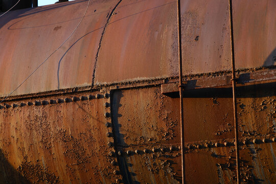 Rivets on a rusting tank with peeling paint at sunset