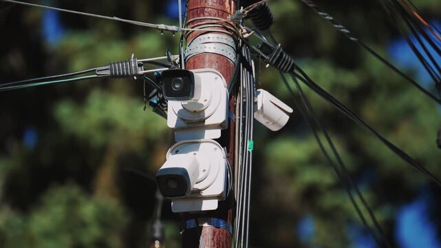 Modern security cameras installed on wooden utility pole with multiple electrical wires and cables.