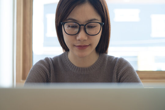 Close up of young asian woman  with eyewear concentrated working on laptop at office. Female student studying online class, searching the information, e-learning