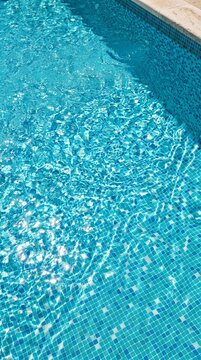 Shimmering turquoise swimming pool water with blue mosaic tiles and sunlight reflections