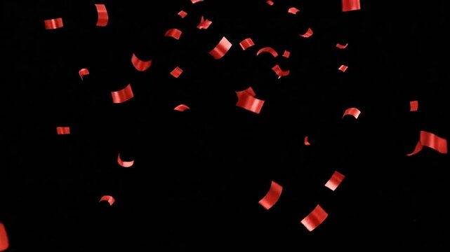 Bright red confetti pieces falling down against a dark black background