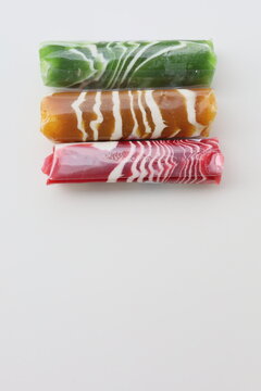 Three pieces of Dodol Garut, traditional Indonesian sweet taffy, with colorful striped patterns in red, green, and brown, isolated on a white background.

