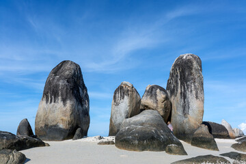 Distinctive upright granite formations known as Batu Berlayar (Sailing Rock) on Belitung Island, Indonesia, rising from white sandy beach under clear blue sky, shaped by natural weathering and coastal © LaTerase