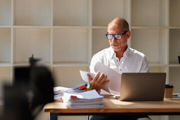 Fototapeta premium Senior businessman managing paperwork and financial documents at office desk