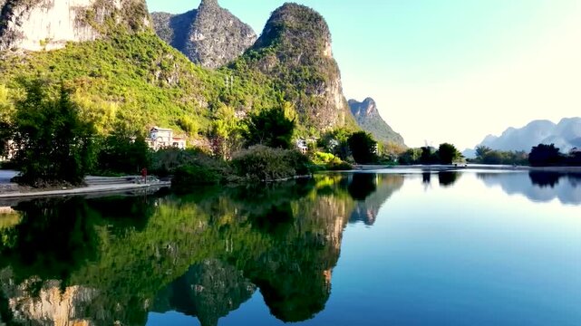 A serene landscape featuring the lush green karst mountains reflecting in the calm river water.