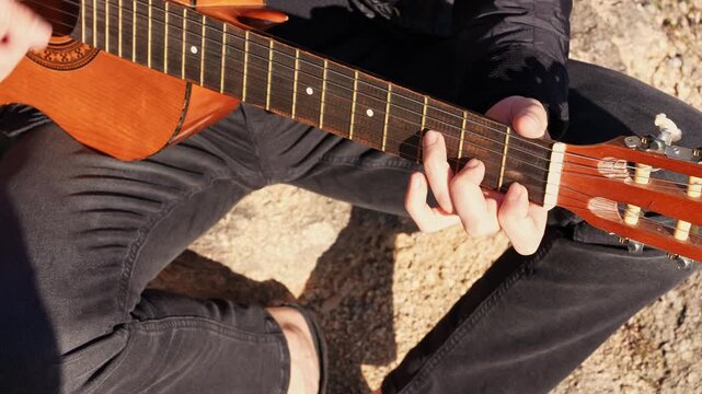 Close up hands of artist plays wooden acoustic guitar in autumnal park. Young songwriter plays string musical instrument hobby outside in nature fall time. Audio music healing in natural surrounding. 