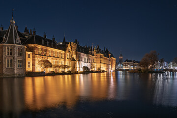 Fototapeta premium Night view of the illuminated Binnenhof government buildings in The Hague, Netherlands, their facades mirrored in the calm Hofvijver pond, blending historic architecture with.