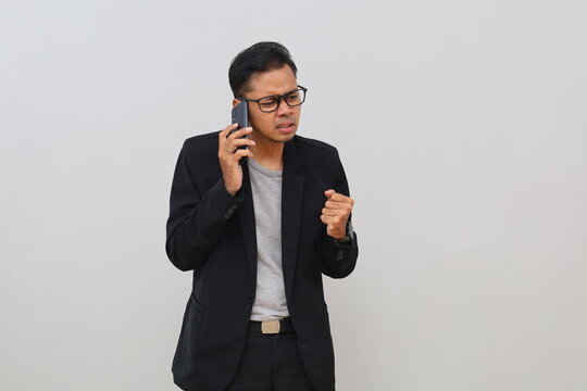 An Asian male businessman is talking on the phone with angry gestures and expressions, looking frustrated, dissatisfied, and wanting to fight, showing negative emotions and tension.