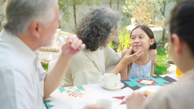 Happy multi generation Asian family enjoy afternoon tea together in garden, grandparent spending time with children and relatives outdoors, family bonding retirement weekend activities lifestyle.