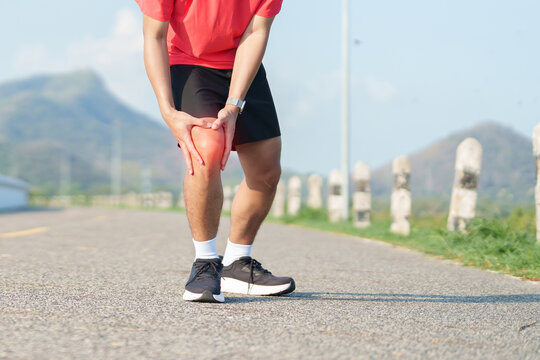 Young adult male runner with knee pain from ACL injury or patellofemoral syndrome. Man having joint ache, ligament tear or patellar tendinitis during running. Sports medical and healthcare concept