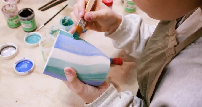 Ceramic art. Pottery class. Unrecognizable talented child hand painting on cup using brush developing creative skill in artisan workshop.