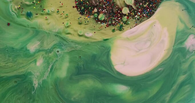 Liquid glitter flow. Ink wave. Defocused green yellow color shiny sequin bright particles oil bubbles floating in water on abstract background.