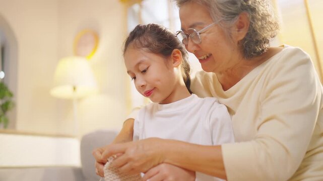 Asian grandmother teaching young granddaughter knitting at home, multi-generation family bonding through leisure activity, elderly woman and child sharing learning and caring relationship