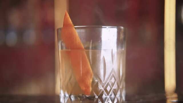 Cocktail glass. Sophisticated drink. Orange beverage serving in crystal with citrus twist on yellow smoke condensation in bar.