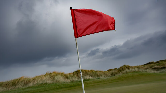 Golf flagstick bending in stormy coastal wind, dramatic low-angle shot
